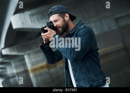 Fotografie Hobby. Junge stilvollen Mann auf der Straße die Bilder auf der Kamera konzentriert Seitenansicht Stockfoto