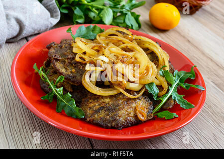 Saftige Scheiben gebratene Leber und Zwiebeln auf einem roten Schild. Stockfoto