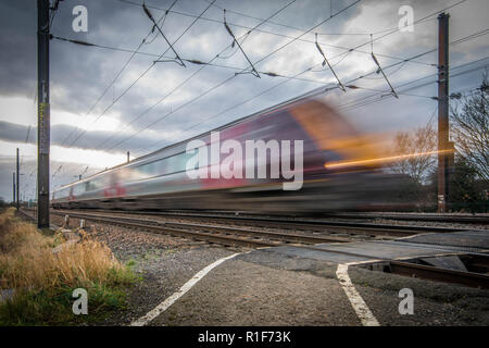 Ein Personenzug Passieren der Kamera mit hoher Geschwindigkeit zu Fuß überqueren. Die dunklen Wolken in den Himmel, um die Dramatik der Szene hinzufügen. Stockfoto