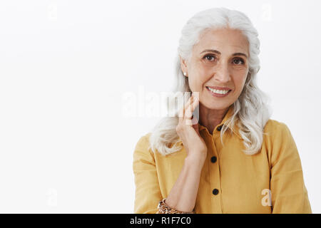 Nahaufnahme der elegante erregt und Gesunde ältere Dame in modischen gelben Fell und Ohrringe berühren, saubere und gesunde Haut mit Nachtcreme sie Anwendung Fältchen zu reduzieren zufrieden sind. Stockfoto