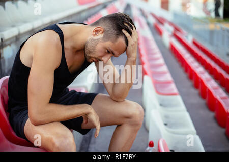 Deprimiert Athlet mann Kopf in den Händen im Stadion sitzen, Stress und traurig Konzept Stockfoto