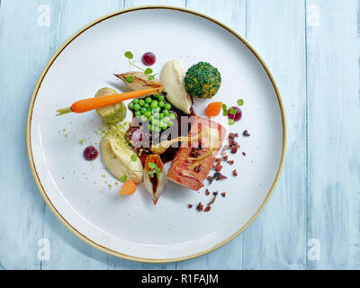 Lende von Kaninchen mit Gemüse gefüllte Knödel und Pease und Karotten auf schwarz-Sauce. Stockfoto