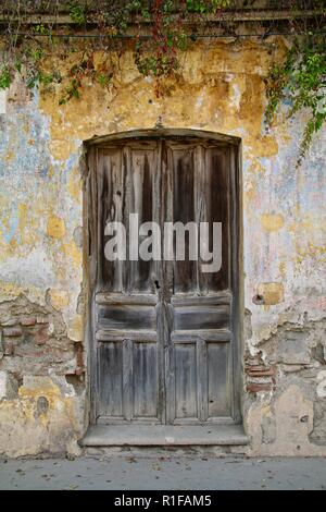 Zentralamerikanischen verwitterten hölzernen Tür in einem gelben und blauen Wand mit Reben an einer ruhigen Straße in Antigua Stockfoto