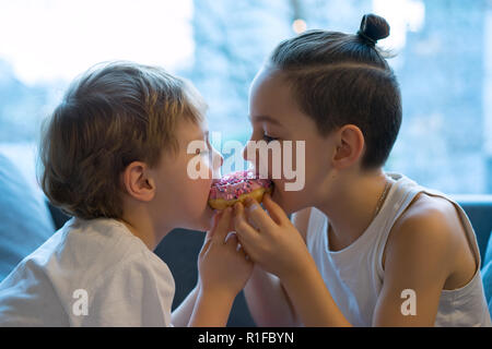 Zwei Kinder Beißen ein Donut und Spaß. zwei Jungen gemeinsam Bissen vom Donut. Kinder einen Donut mit Erdbeer bereifen genießen. Teilen Sie die einen Donut ich Stockfoto