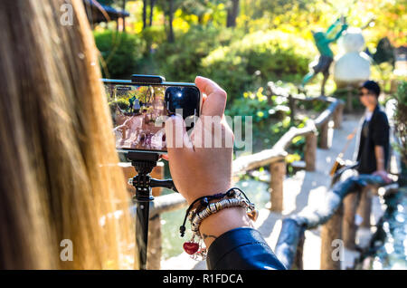 Über die Schulter geschossen als eine Dame, ein Foto von ihrem Freund ein iPhone Smartphone dauert. Stockfoto