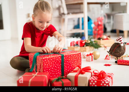 Cute Super aufgeregt, junges Mädchen Öffnen großer rot Weihnachtsgeschenk sitzend Wohnzimmer Erdgeschoss. Ehrliche Familie Weihnachten lifestyle backgroun Stockfoto