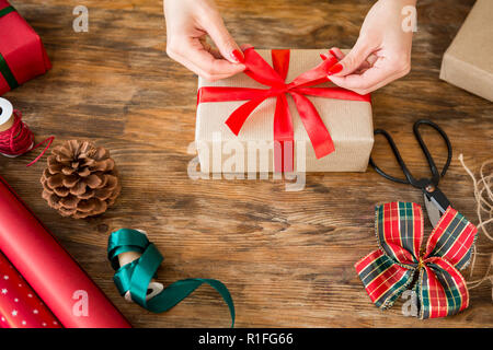 DIY Geschenkverpackung. Frau Verpackung schöne Weihnachtsgeschenke auf rustikalen Holztisch. Ansicht von Weihnachten folierstation. Stockfoto