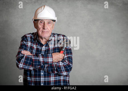 Älterer Mann mit einem weißen Helm mit einem Schraubenschlüssel auf grauem Hintergrund Stockfoto