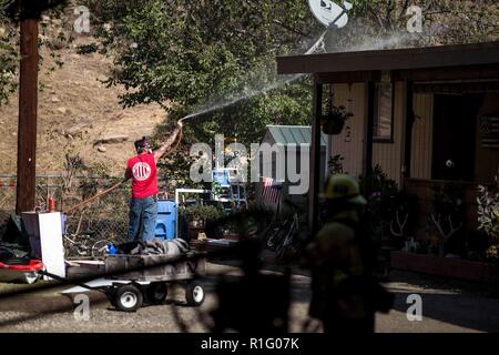 Simi Valley, Kalifornien, USA. 12 Nov, 2018. Ein Mann versucht, sein Haus mit einem Gartenschlauch zu nass, um sein Eigentum zu schützen. Quelle: Chris Rusanowsky/ZUMA Draht/Alamy leben Nachrichten Stockfoto