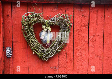 Traditionelle Handarbeit Zweig Herzen hängen auf roten Holztür mit Klopfer. Stockfoto