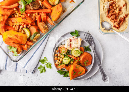 Gebackene Gemüse (Karotten, Zucchini, Kartoffel, Kürbis) mit Kichererbsen und Hummus, Ansicht von oben. Auf Basis pflanzlicher Ernährung Konzept. Stockfoto