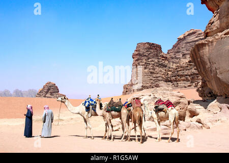 Zwei Beduinen in traditioneller Kleidung mit vier Kamele Dromedare Wüste im Wadi Rum, Jordanien, Naher Osten Stockfoto