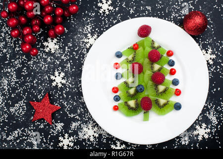 Genießbare Weihnachtsbaum von Kiwi Slices auf einer schwarzen Platte über Dunkle Schiefer, Stein oder Beton Hintergrund Stockfoto