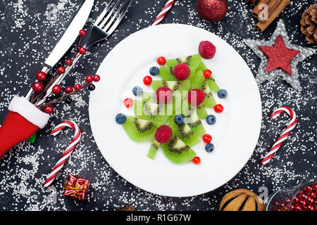 Genießbare Weihnachtsbaum von Kiwi Slices auf einer schwarzen Platte über Dunkle Schiefer, Stein oder Beton Hintergrund Stockfoto