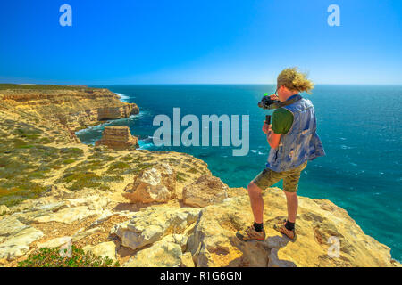 Reisen Fotograf mit Gimbal der Insel Rock im Kalbarri Nationalpark, Western Australia schoß nimmt, an einem sonnigen Tag mit blauen Himmel. Professionelle videomaker nimmt Foto des Australischen Coral Coast. Stockfoto