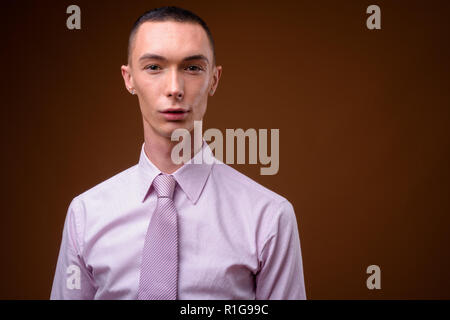 Junge schöne androgyne Geschäftsmann gegen braunen Hintergrund Stockfoto