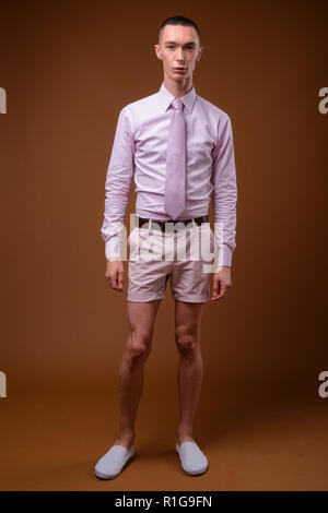 Junge schöne androgyne Geschäftsmann gegen braunen Hintergrund Stockfoto