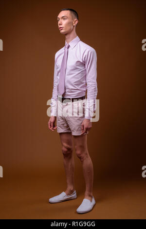 Junge schöne androgyne Geschäftsmann gegen braunen Hintergrund Stockfoto