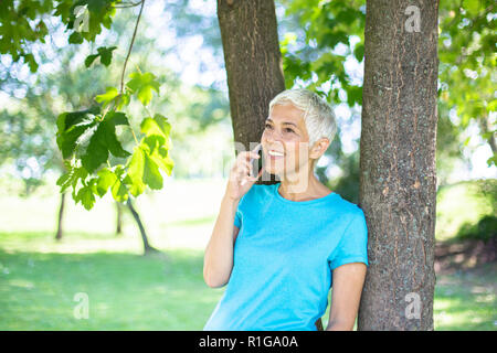 Portrait von sportlichen ältere Frau mit Handy im Park an einem sonnigen Tag Stockfoto