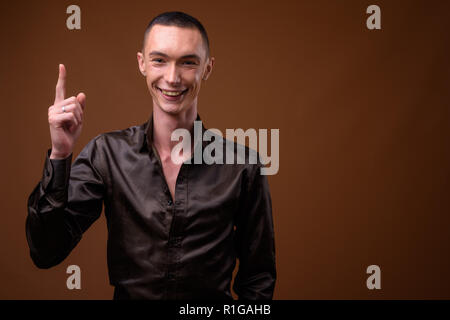 Junge schöne androgyne Geschäftsmann gegen braunen Hintergrund Stockfoto