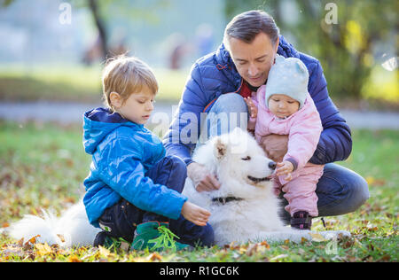 Vater mit Sohn und Tochter spielen mit samojeden Hund im Herbst Park Stockfoto