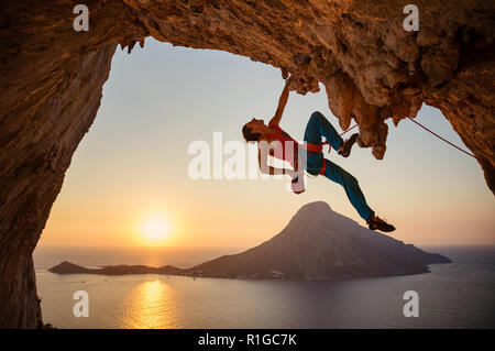 Männliche Kletterer hängen mit einer Hand auf die anspruchsvolle Strecke auf einer Klippe und Kreide auf ein anderes Stockfoto