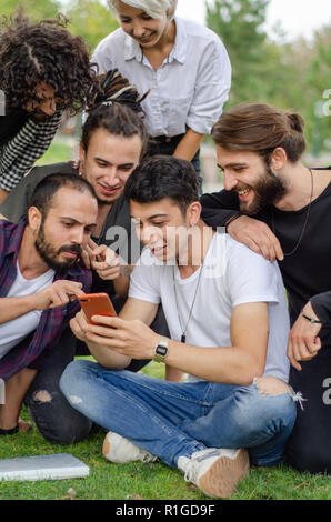 Eine Gruppe junger Leute arbeiten im Park mit Handys. Sie sehen gerade Spaß Dinge am Telefon. Stockfoto