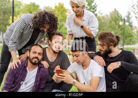 Eine Gruppe junger Leute arbeiten im Park mit Handys. Sie beobachten das Telefon vorsichtig. Stockfoto