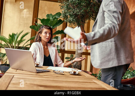 Business Lunch. Frau sitzt am Tisch, während man standing Hände beiseite argumentieren irritiert close-up Stockfoto