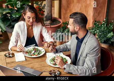 Business Lunch. Der Mann und die Frau am Tisch sitzen im Restaurant essen gesund frischer Salat sprechen lächelt fröhlich Top View Stockfoto