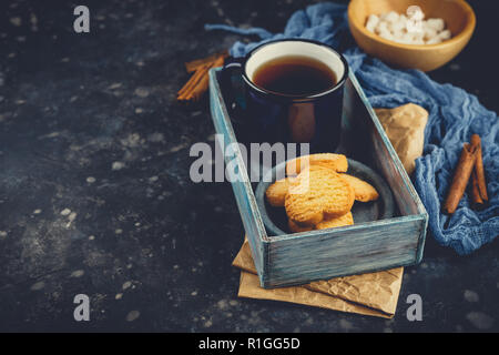 Blau emailliert Tasse Tee, Zimtstangen, Anis Sterne und Shortbread auf einem dunklen Hintergrund. Platz für Text. Stockfoto