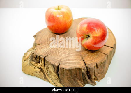 Rote Äpfel auf einem Baumstumpf auf weißem Hintergrund. Stück Holz kreuz sectionwith Baum ring Textur, Muster und Risse. stehen für Innenausstattung. Gesunde Ernährung. Diät Konzept Stockfoto