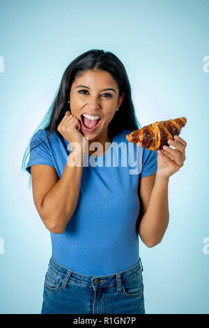 Schöne junge niedlich und Latin Frau in Freizeitkleidung Holding Big leckere Schokolade Croissant mit Versuchung denken wenn Ignorieren di Stockfoto