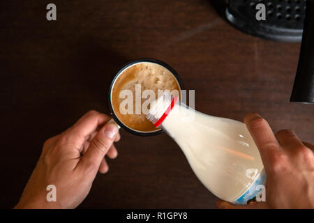 Foto der Kaffeemaschine, die Hände des Menschen gießen Milch in die kaffeetasse Stockfoto