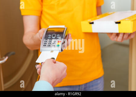 Foto von Kurier in gelben T-Shirt mit Box mit Pizza und Point-of-Sale Stockfoto