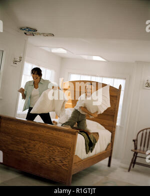 Reife Frau in kissenschlacht auf dem Bett mit ihrem Sohn. Stockfoto