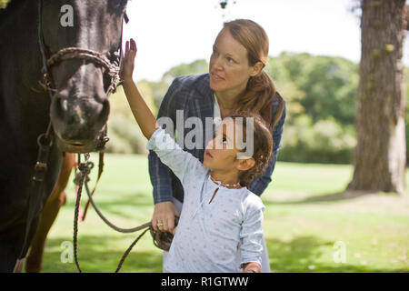 Mitte der erwachsenen Frau und ihre junge Tochter mit einem Pferd draußen. Stockfoto