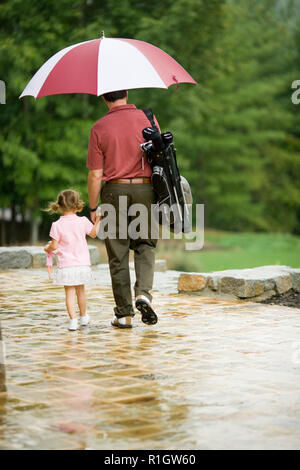 Junge Mädchen, dass Mitte des erwachsenen Vater Hand wie der Spaziergang mit einem Golf Bag und ein Regenschirm. Stockfoto