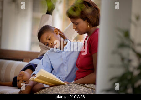 Porträt eines Jungen mit der Oberseite nach unten auf einer Couch neben seinem älteren Bruder, der mit seinem mittleren - Erwachsene Mutter. Stockfoto