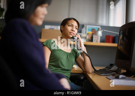 Schwere Mid - erwachsene Frau mit einem Telefonhörer an Ihr Ohr beim Sitzen in einem Büro mit ihrem Kollegen. Stockfoto