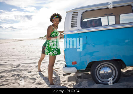 Portrait einer jungen Frau steht neben einem van am Strand. Stockfoto