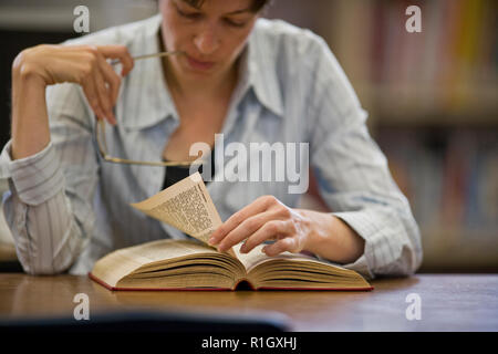 Konzentrierte sich Mitte der erwachsenen Frau mit einem Buch in einer Bibliothek. Stockfoto