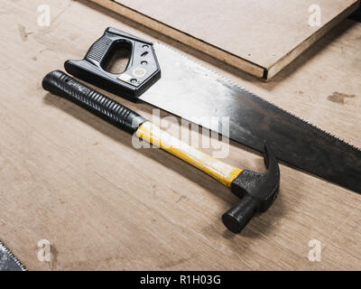 Hammer, Säge, und Holzbrett auf einem Holztisch in der Werkstatt Raum platziert Stockfoto