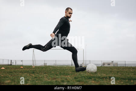 Fußballspieler, der an einem bewölkten Tag auf dem Spielfeld seine Kicks trainiert. Mann spielt Fußball auf dem Feld, der gerade den Ball kickt. Stockfoto