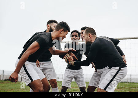 Fußballspieler halten ihre Hände in einer Keule stehend und feuern sich an. Fußballer, die in der Nähe des Torpfosten stehen, in einem Huddle, die einen Pep ta haben Stockfoto