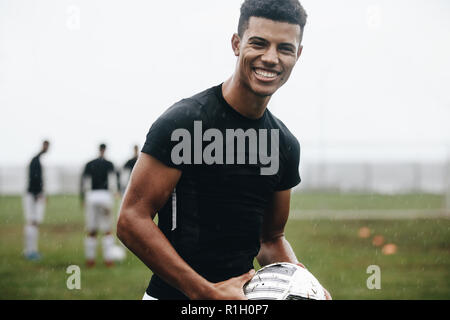 Porträt eines lächelnden footballer stehen auf Feld in Regen. Fröhliche Fußball-Spieler üben in den Morgen auf Feld mit Mannschaftskameraden spielen in der Ba Stockfoto