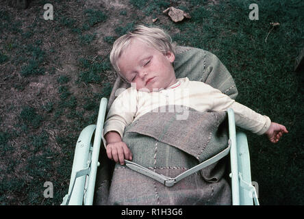 1960, historische, ein blonder Junge schlafend unter einem wollenen Teppich außerhalb liegen in einem kleinen Kinderwagen, England, UK. Stockfoto