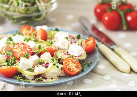 Gesund lecker lecker Salat mit Tomaten, Radieschen, Käse, Sprossen und Sesam in der Platte auf hellem Holztisch, flacher Tiefe des Feldes. Stockfoto