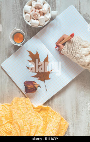Frau Hand schreiben in Notepad, Tasse Kaffee, getrocknete Rose und Herbst Blatt. Herbst Winter schönen Hintergrund, gemütliche Home Konzept, kopieren. Stockfoto