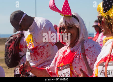 Gemischte Rasse Frau tragen ein Paar von pink Polka Dot Hasenohren und blonde Perücke Lächeln auf die Kamera zu Fuß mit einer Gruppe von Freunden in Fun Run Sport Event Stockfoto